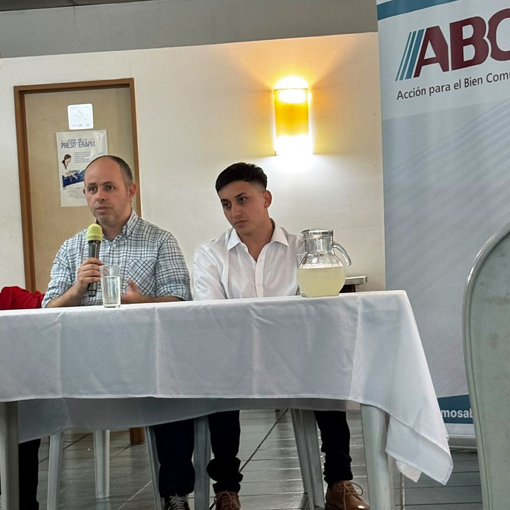 Charla de ABC con micrófono, frente al banner del partido